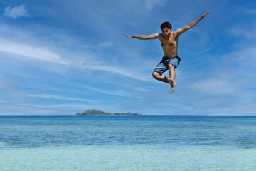 Young man jumping in the air at the beach of Raja Ampat. Carefree people vacation time concept...