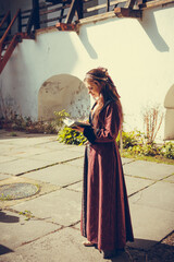 Portrait of brunette woman dressed in historical Baroque clothes  reading book, outdoors. Middle class medieval dress