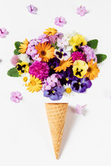 Ice cream waffle cone with colorful vibrant flowers on white background. Flat lay, top view. Minimal summer creative concept.