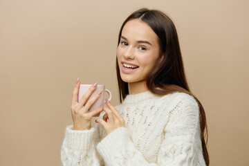 joyful, happy woman stands in a white sweater on a beige background and pleasantly smiling at the camera holds her pink cup with both hands