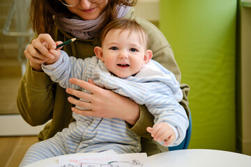 A mother woman with a toddler baby boy draws while waiting for a doctor during a visit to a...