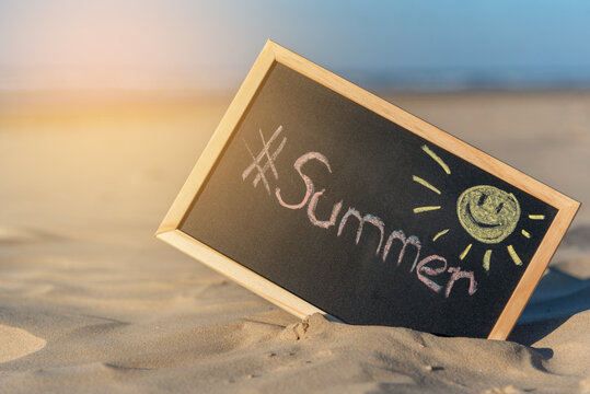 Una pizarra negra con un sol dibujado y escrita la palabra summer, en la arena de una playa con la luz del sol dándole desde arriba. símbolo que refleja el verano. pizarra negra de escuela. 