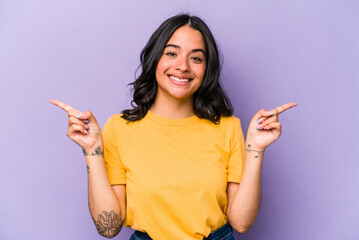 Young hispanic woman isolated on purple background pointing to different copy spaces, choosing one of them, showing with finger.