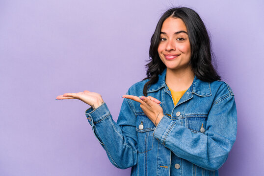 Young hispanic woman isolated on purple background excited holding a copy space on palm.