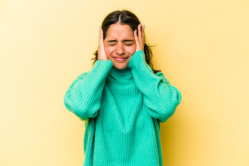 Young hispanic woman isolated on yellow background covering ears with hands.