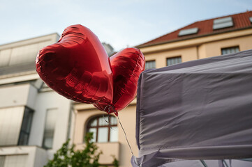 Zwei rote Luftballons in Herzform schweben vor einer Häuserfront einer städtischen Umgebung