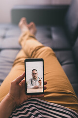 Woman lying on a sofa and talking with a doctor online using mobile phone. Telemedicine concept. - obrazy, fototapety, plakaty