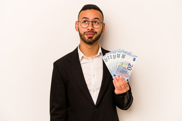 Young business hispanic man holding banknotes isolated on white background dreaming of achieving goals and purposes