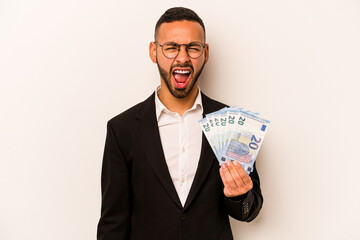 Young business hispanic man holding banknotes isolated on white background screaming very angry and aggressive.