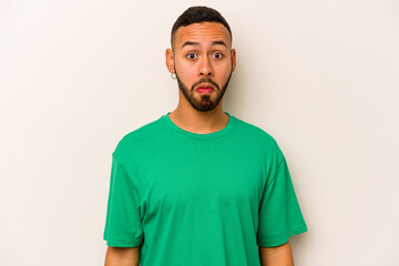 Young hispanic man isolated on white background shrugs shoulders and open eyes confused.