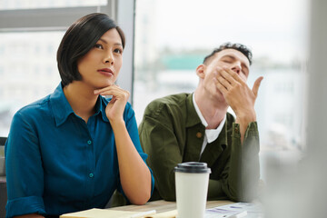 Businesswoman listening speaker with interest when her coworker is yawning at business training