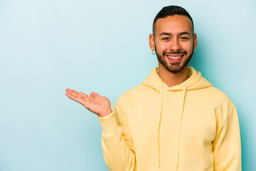 Young hispanic man isolated on blue background showing a copy space on a palm and holding another...