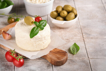 Ricotta cheese. Homemade Ricotta cheese with basil, garlic, tomatoes and green olives on parchment paperback and stand on old beige tiles background. Italian food. Selective focus.