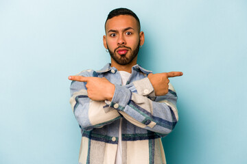 Young hispanic man isolated on blue background points sideways, is trying to choose between two options.