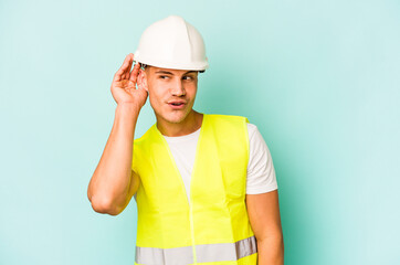 Young laborer caucasian man isolated on blue background trying to listening a gossip.