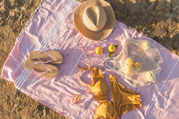 Summer beach accessories flat lay on sand background. Holiday travel, tropical concept. Straw hat, bikini, sunglasses, slippers and fruits in eco friendly mesh shopping bag. Sun shadow and sunlight