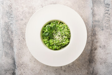 Italian risotto. Delicious risotto in white plate with pesto sauce or wild garlic pesto, basil, parmesan cheese and glass of white wine on old light grey table background. Top view with copy space.