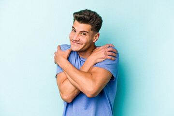 Young caucasian man isolated on blue background hugs, smiling carefree and happy.