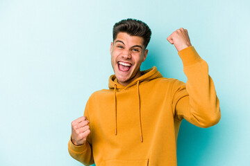 Young caucasian man isolated on blue background cheering carefree and excited. Victory concept.