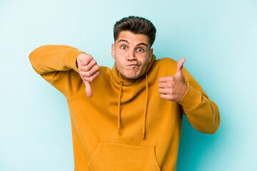 Young caucasian man isolated on blue background showing thumbs up and thumbs down, difficult choose concept