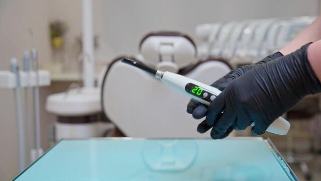 A dentist's assistant in black gloves shows how to work properly with a polymerization lamp in a medical office. A lesson for dentists and their assistants.