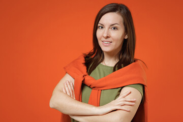 Obraz premium Young smiling happy fun woman 20s wearing khaki t-shirt tied sweater on shoulders look camera hold hands crossed folded isolated on plain orange background studio portrait. People lifestyle concept.