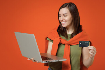Young happy woman 20s wear khaki t-shirt tied sweater on shoulders using laptop pc computer hold...