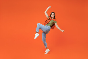 Fototapeta na wymiar Full body young excited fun happy woman 20s wearing khaki t-shirt tied sweater on shoulders doing winner gesture celebrate clenching fists say yes isolated on plain orange background studio portrait