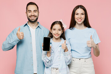 Young fun parents mom dad with child kid daughter teen girl in blue clothes hold use mobile cell phone screen workspace area show thumb up isolated on plain pastel pink background. Family day concept.