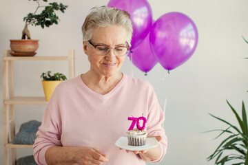 Elderly smiling cool happy woman 70s hold birthday cake with candle