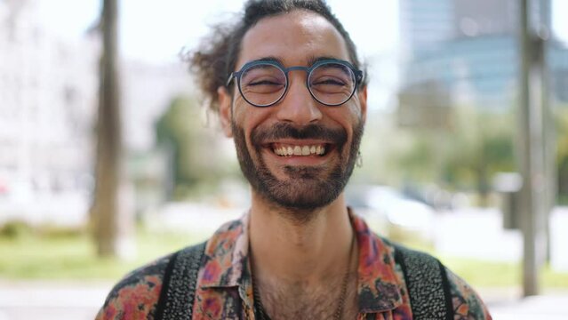 Smiling curly-haired bearded man in eyeglasses looking at the camera outdoors