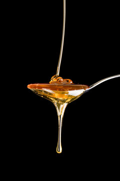 Honey dripping in silver spoon, black background.