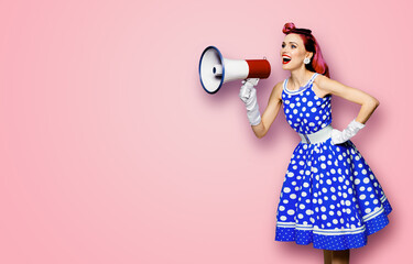 Purple haired woman holding red megaphone, shout advertising something. Girl in blue pin up style with mega phone loudspeaker. Rose pink background with mock up. Female model in retro fashion dress.