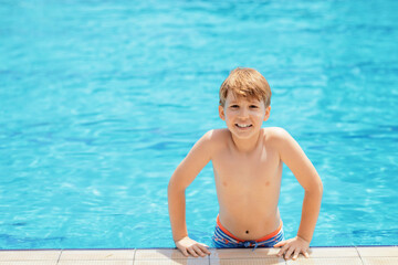Smiling cute little boy in outdoor swimming pool in sunny day. Water activities for kids at holidays.