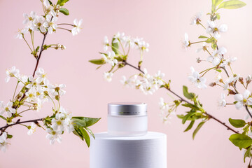 jar of cream on a white round podium and twigs of cherry blossoms on a beige background