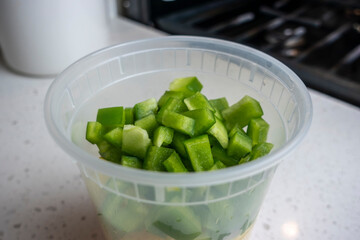 View of coloful diced bell peppers in a plastic container on a kitchen counter, prepped for cooking