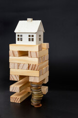 Model house on top of a wood blocks tower, supported by a high stack of coins