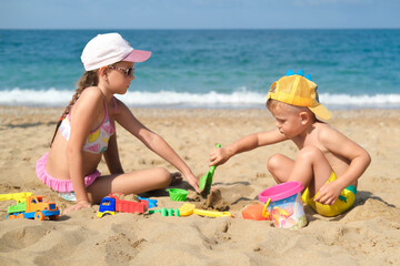 Brother and sister play on the beach with plastic toys with sand. Children are playing on the beach. Summer water fun for the whole family. A boy and a girl are playing with sand on the seashore.