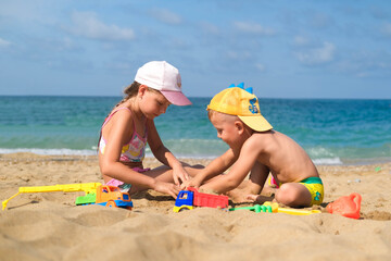 Brother and sister play on the beach with plastic toys with sand. Children are playing on the beach. Summer water fun for the whole family. A boy and a girl are playing with sand on the seashore.
