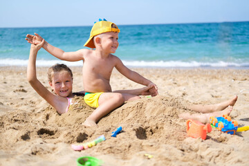 Brother and sister play on the beach with plastic toys with sand. Children are playing on the beach. Summer water fun for the whole family. A boy and a girl are playing with sand on the seashore.