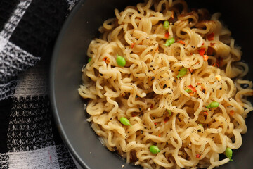 Noodles in a bowl with peas and chilli flakes. Sugar snap peas and red chilli in background 