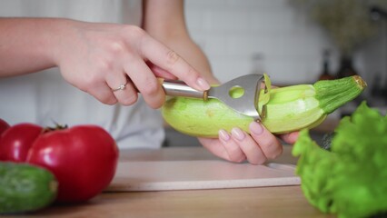 Close-up of an unrecognizable woman's hand peeling a zucchini with a vegetable peeler. Cooking in the kitchen.