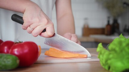 Close-up of an unrecognizable woman's hand cutting a carrot with a kitchen knife. Cooking in the kitchen.
