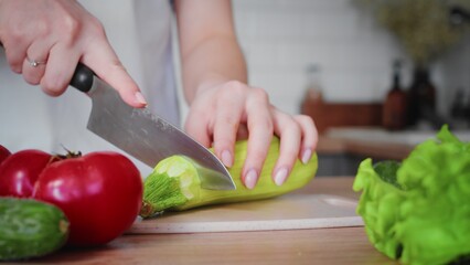 Close-up of an unrecognizable woman's hand cutting a zucchini with a kitchen knife. Cooking in the kitchen.