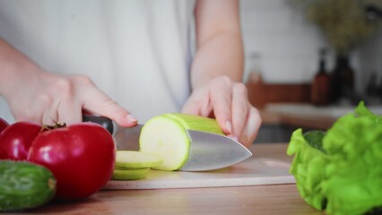 Close-up of an unrecognizable woman's hand cutting a zucchini with a kitchen knife. Cooking in the kitchen.