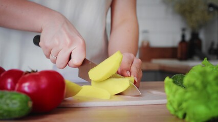 Close-up of an unrecognizable woman's hand cutting potatoes with a kitchen knife. Cooking in the kitchen.