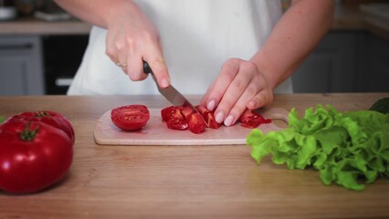 Close-up of an unrecognizable woman's hand cutting a tomato with a kitchen knife. Cooking in the kitchen.