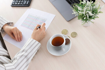 Top view of woman's hands above the calculating manage expenses expenditures paying bills on laptop with cup of tea.