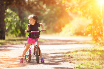 Happy cute girl with bicycle in the summer park. Beauty nature scene with healthy outdoor lifestyle. Happy kid having fun outdoor at summer. Happiness and harmony - 507886186