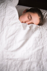 Chica durmiendo en una cama con colcha blanca.